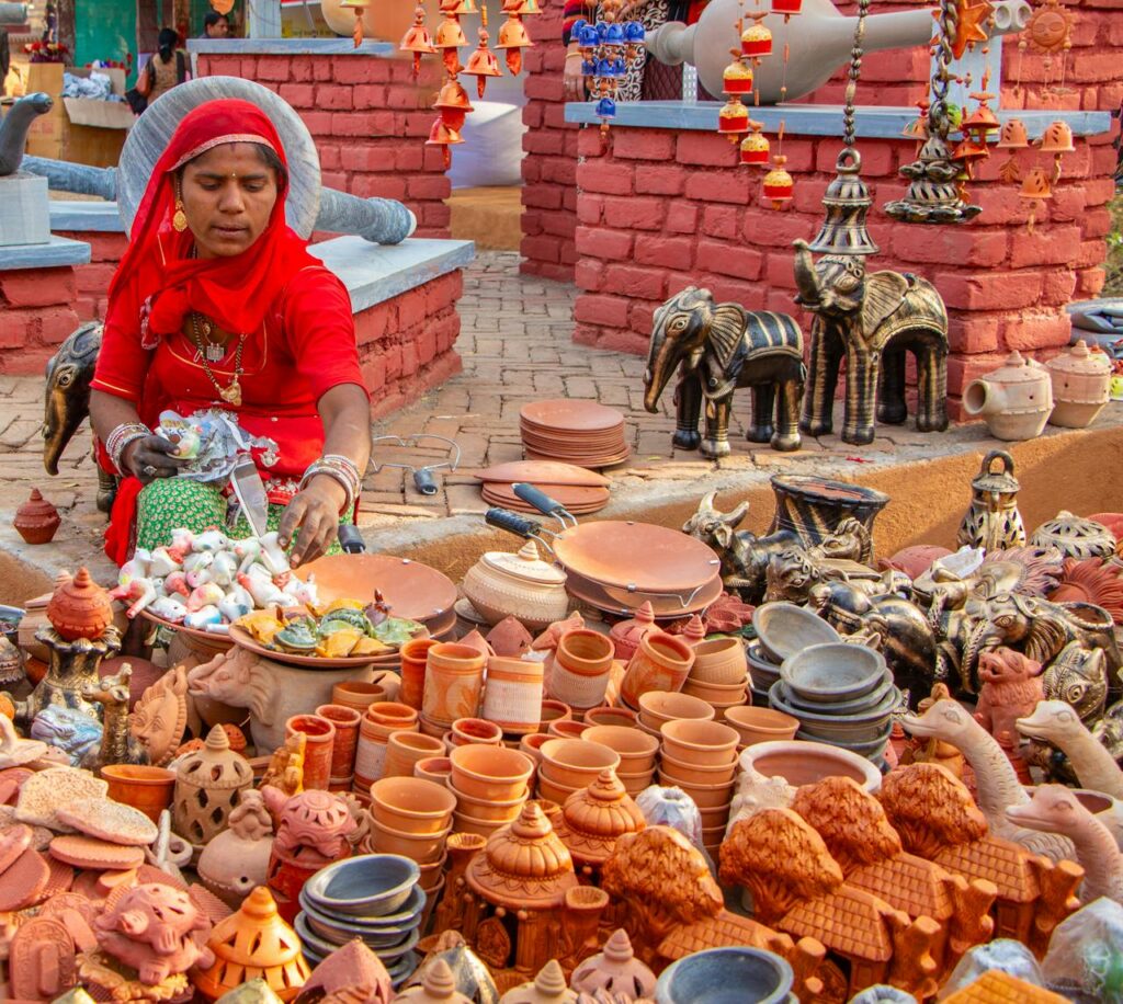 A vibrant display of handmade pottery sold by a woman in traditional clothing at a Jaipur market.
